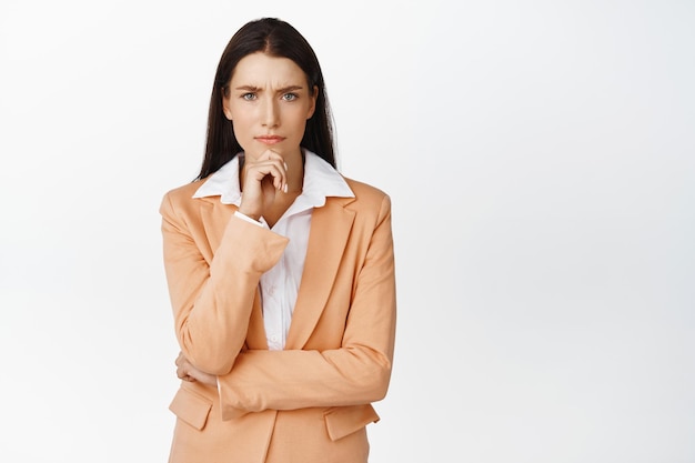 Image of businesswoman looking concerned thinking with frowned troubled face solving problem standing in suit against white background