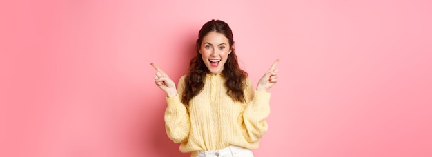 Free Photo image of cheerful goodlooking female model pointing fingers aside showing two choices sidewas left a