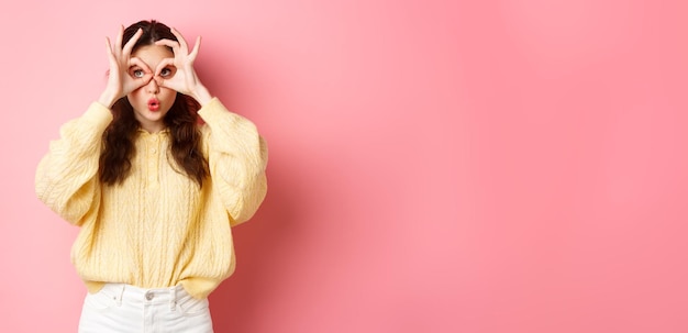 Free photo image of cute surprised girl looking through hand binoculars staring at upper left corner and saying