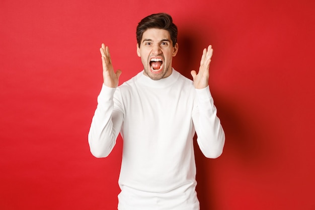 Image of frustrated and angry man in white sweater shouting in rage being mad at someone standing ov...