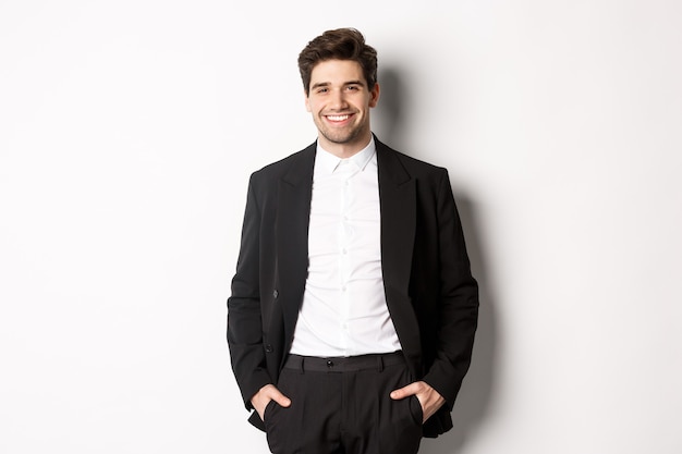 Image of handsome caucasian man in party suit, smiling pleased, attend formal event, standing over white background