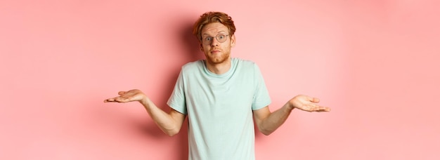 Free photo image of handsome redhead man in glasses and tshirt know nothing shrugging shoulders and raising eye