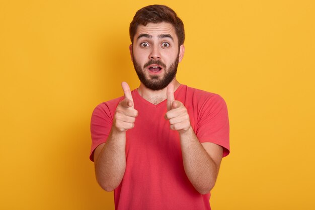 Image of handsome young man standing isolated over yellow, looking at camera and pointing with fore fingers