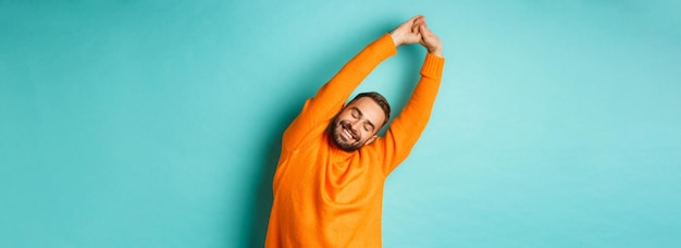 Free photo image of handsome young man stretching hands and smiling after good rest standing in orange sweater