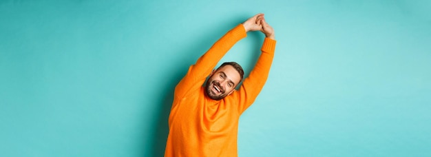 Free photo image of handsome young man stretching hands and smiling after good rest standing in orange sweater