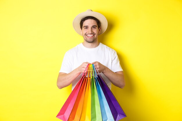 Image of happy man shopping on vacation, holding paper bags and smiling, standing against yellow background