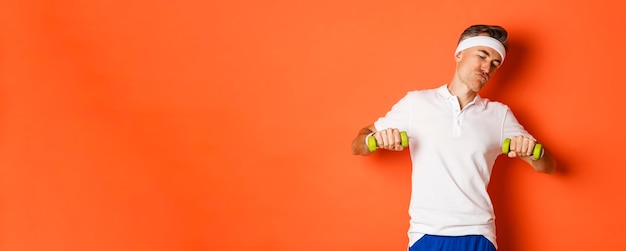 Free photo image of happy middleaged guy doing sports workout with dumbbells standing over orange background