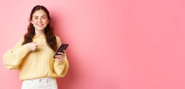 Free Photo image of happy smiling young woman holding mobile phone and pointing at mobile screen with pleased a