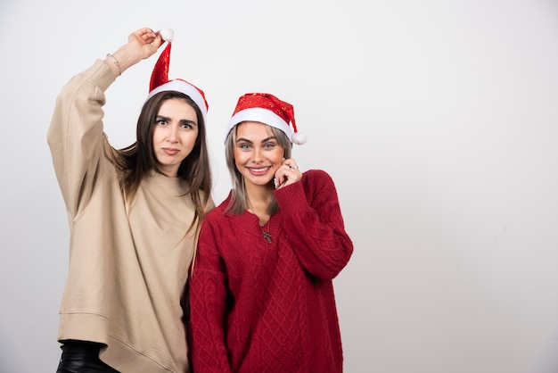 Image of a happy woman holding a Santa hat near her pretty women friend .