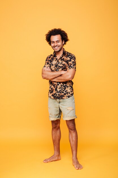 Image of happy young african man standing and posing over yellow wall with arms crossed. 