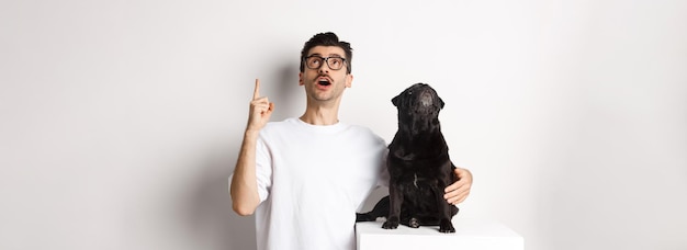 Free photo image of happy young man and dog both looking up at promo owner pointing finger at top pug staring a