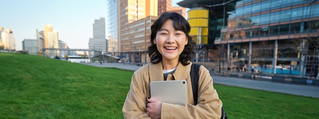 Free photo image of korean girl with happy face walks around town with student tablet stands on street and