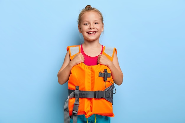 Free photo image of lovely ginger girl wears protective lifejacket, enjoys safe summer vacation, favourite season