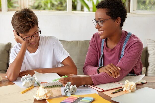 Image of mixed race boy and girl collaborate for preparing course paper, make records in notepad, sit at couch, work on presentation for class, being team. Learning and collaboration concept