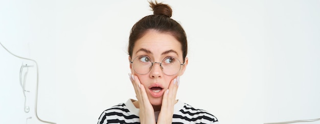 Free photo image of shocked woman in glasses holds hands on face gasps and looks speechless amazed by news