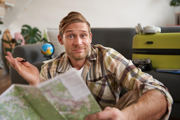 Free Photo image of shrugging man with road travel map looks at camera with confused face packs suitcase for