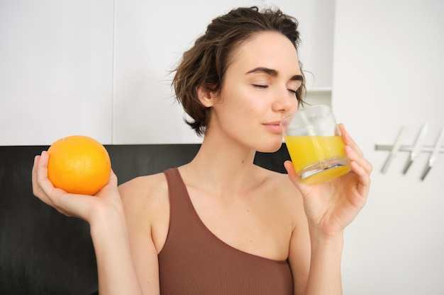 Free photo image of sportswoman fitness girl holding glass of juice and an orange smiling drinking vitamin beve