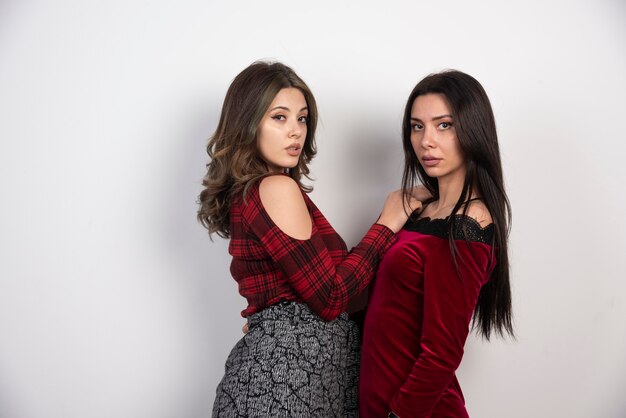 Image of two best friends standing together and looking at camera on white wall .