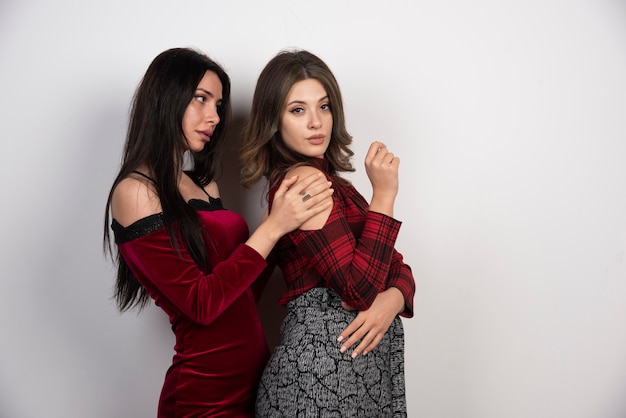 Image of two young beautiful girls standing and posing on white wall .