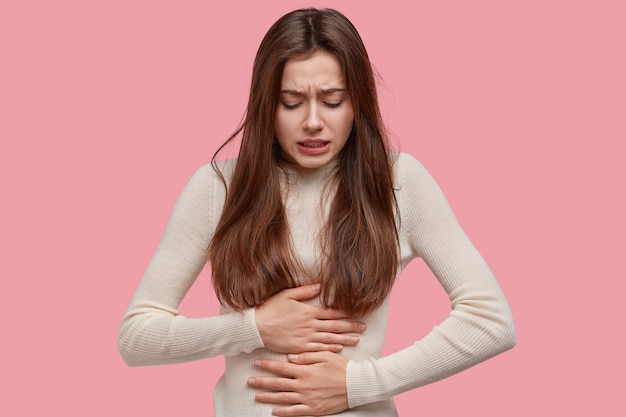 Free photo image of unhappy woman suffers from stomachache after eating spoiled food, feels discomfort in belly, has disorder