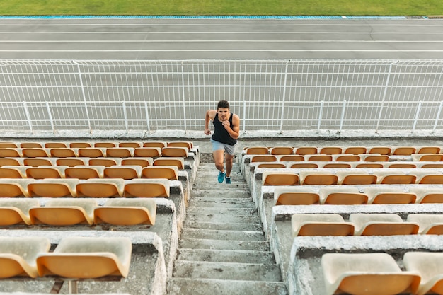 Free photo image of young athletic man running by ladder at the stadium out