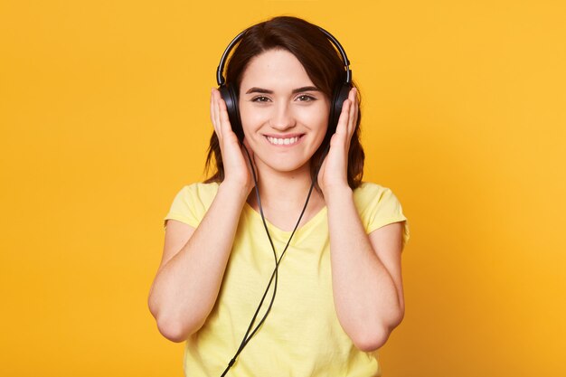 Image of young happy woman with headphones listening to music isolated over yellow