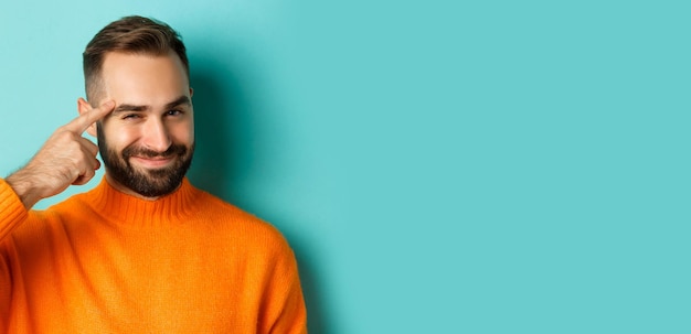 Free photo image of young man in orange sweater smiling and pointing at head having an idea praising good thoug