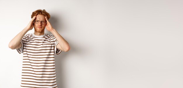 Free Photo image of young man with red hair and glasses touching head frowning from painful migraine having hea