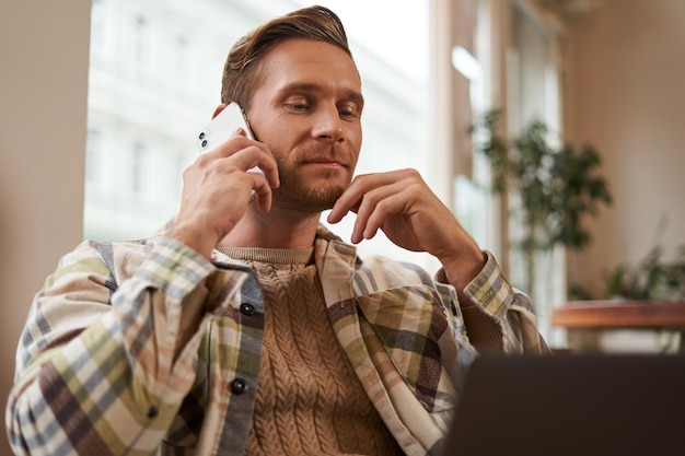 Free Photo image of young professional cafe visitor working sitting with laptop and talking on mobile phone to