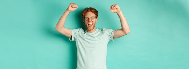 Free photo image of young redhead man feeling like champion raising hands up in fist pump gesture and shouting