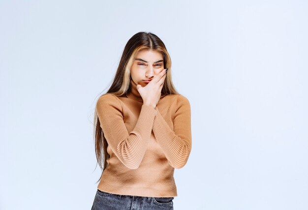 Image of a young woman model in brown sweater standing and holding cheek.