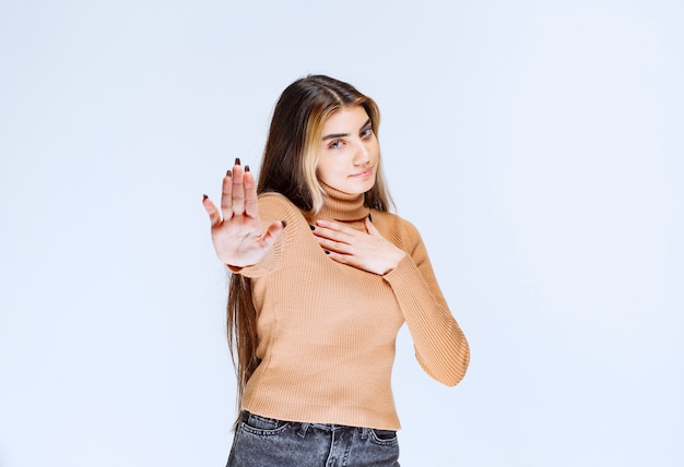 Image of a young woman model in brown sweater standing and making stop sign .