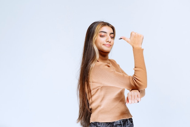 Image of a young woman model in brown sweater standing and pointing away.