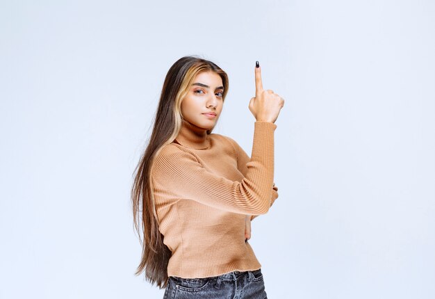 Image of a young woman model in brown sweater standing and pointing up.