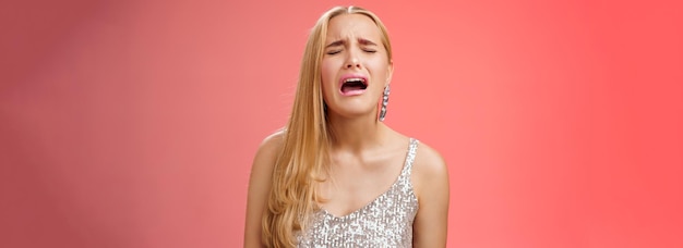 Free Photo immature whining spoiled adult rich daughter blond long hair in silver stylish dress complaining sad cruel unfair life crying sobbing frowning sulking upset standing disappointed red background