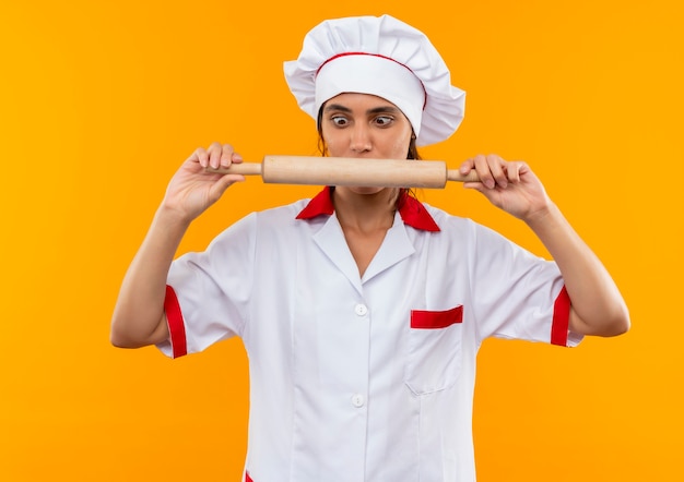 Free photo impresed young female cook wearing chef uniform holding and looking at rolling pin on isolated yellow wall