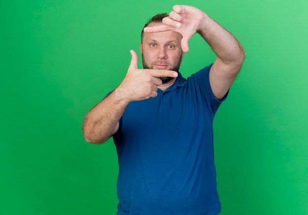 Impressed adult slavic man  and doing frame gesture isolated on green wall with copy space