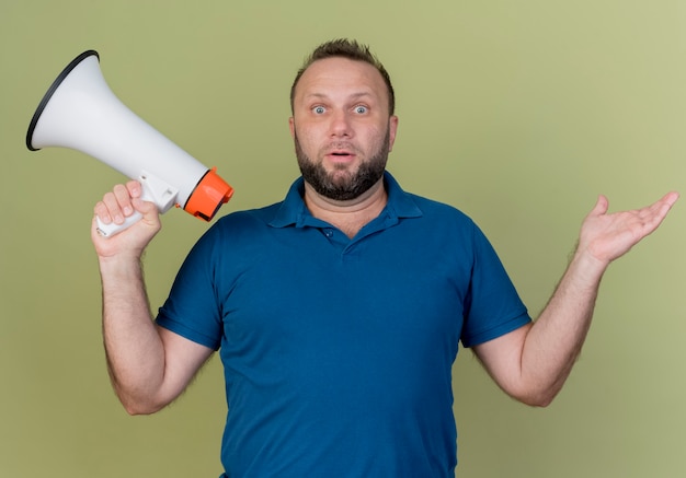 Free Photo impressed adult slavic man holding speaker and showing empty hand 