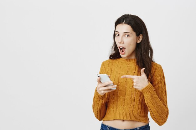 Impressed girl found great app, pointing finger at smartphone