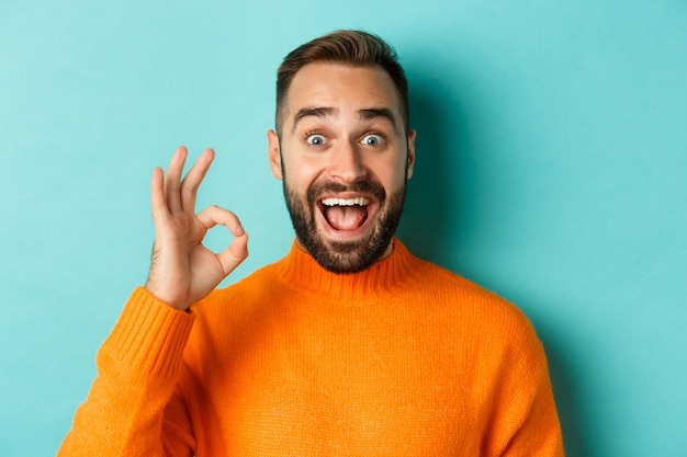 Impressed handsome man showing okay sign, recommending something good, praising with ok gesture