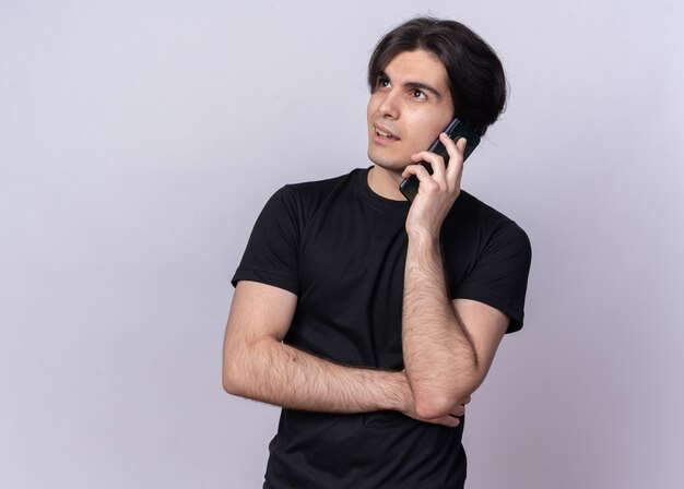 Impressed looking at side young handsome guy wearing black t-shirt speaks on phone isolated on white wall