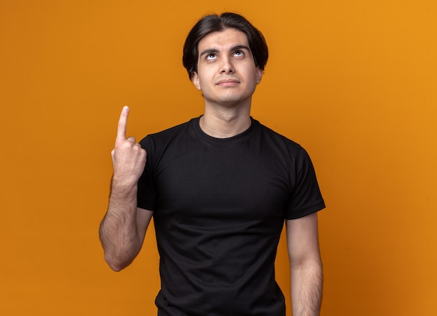 Free photo impressed looking up young handsome guy wearing black t-shirt points at up isolated on orange wall