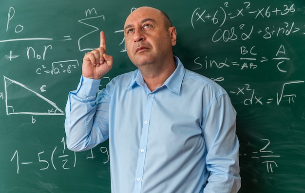 Free Photo impressed middle-aged male teacher standing in front blackboard points at up