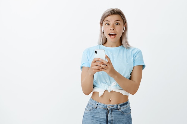 Impressed and pleased blonde girl posing in the studio with her phone and earphones