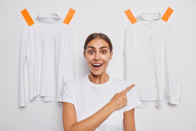 Free photo impressed surprised cheerful young european woman indicates at shirt plastered to background cannot believe her eyes demonstrates clothes to wear advertises something. wow look on this shirt.