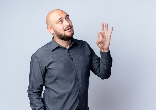 Impressed young bald call center man looking up and doing ok sign isolated on white  with copy space