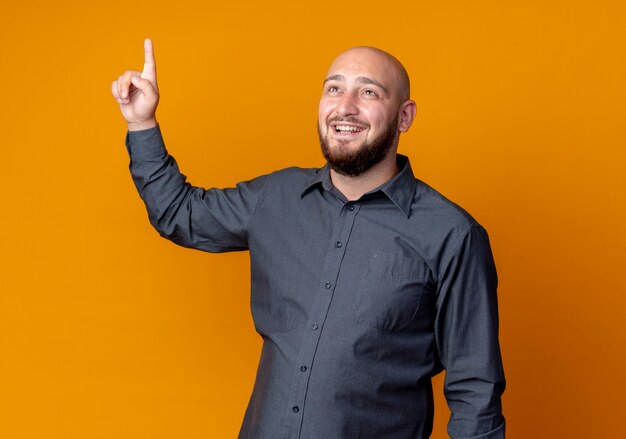 Impressed young bald call center man looking up with raised finger isolated on orange 