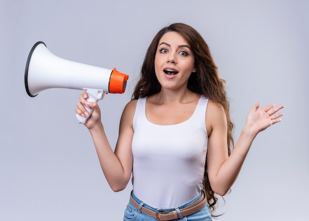 Impressed young beautiful girl holding speaker and showing empty hand 