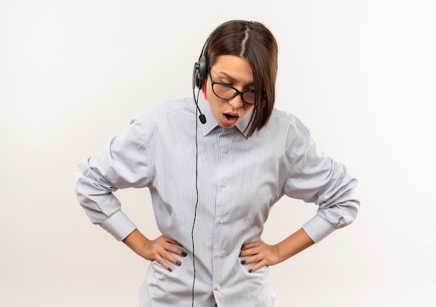 Free photo impressed young call center girl wearing glasses and headset putting hands on waist looking down isolated on white  with copy space