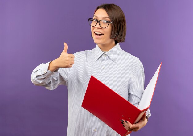 Impressed young call center girl wearing glasses holding folder showing thumb up isolated on purple 